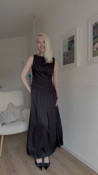 Musta mekko, jossa on teksturoitu, rypistynyt yläosa ja valuva hame. Satiinikangas, jossa on sileä pinta. Yhdistetty mustiin korkokenkiin.