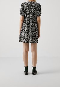 Černé šaty s bílým vzorem růží, krátké balónové rukávy, vyhovující pas a rozšířená sukně. Nosené s černými plochými botami se cvočky a zelenými ponožkami.