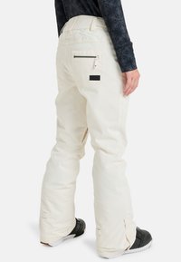 Weiße Schneehosen mit lockerer Passform, strapazierfähigem Stoff, seitlichem Reißverschluss-Taschen und verstellbaren Bündchen. Mit einem Logo-Patch auf der Rückseite.