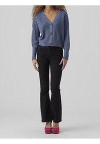 Blå stickad cardigan med V-hals, knappstängning och långa ärmar, combinarad med svarta utsvängda jeans och rosa platåskor.