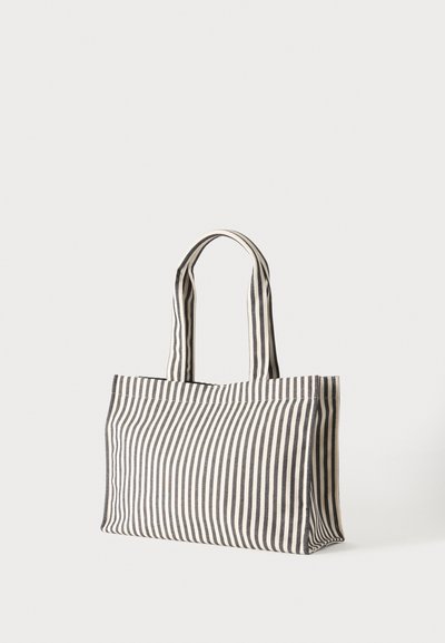 Sac fourre-tout en toile avec des rayures verticales noires et blanches et deux longues poignées sur un fond clair uni.