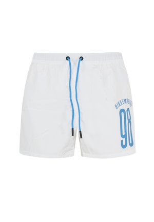 Witte zwembroek met een blauwe trekkoord en een groot blauw '98' print aan de zijkant, gecombineerd met zwarte sandalen, gedragen door een staande mannelijke model.