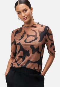 Blouse transparente marron avec imprimé animal abstrait noir, manches courtes et encolure festonnée. Le tissu a une apparence légère et texturée.