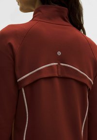 Giacca sportiva rossa con colletto alto, cuciture bianche a contrasto e un logo sul retro, progettata con un dettaglio posteriore a strati.