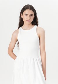 White sleeveless dress with a fitted ribbed bodice and flared skirt. Soft texture, smooth fabric, and a round neckline with no embellishments.