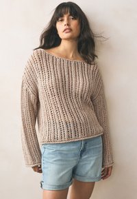 Beige strikket sweater med åben vævning, bådhalsudskæring og løse ærmer, kombineret med lyseblå denimshorts med opsmøgede kanter.