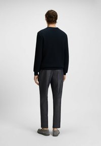 Navy textured sweater with round neckline, paired with gray patterned trousers. Model stands with back facing the camera. Gray slip-on shoes.