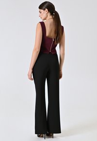 Top bordeaux senza maniche con schiena bassa e dettaglio con zip, abbinato a pantaloni a gamba larga neri e scarpe con tacco alto. Texture del tessuto liscia.