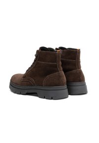 Botas de tobillo de ante marrón con una suela de goma negra duradera. Las características incluyen ojales reforzados, costuras en contraste y una etiqueta multicolor.