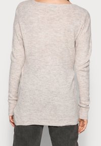 Pull en maille beige clair avec une coupe ample, un col large et des manches longues. Tissu texturé avec des variations subtiles de couleur.