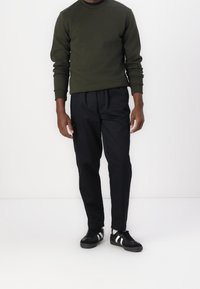 Olivgrön sweatshirt med rund hals, svarta tapered byxor med sidofickor och svarta skor med vita ränder. Slät textur, avslappnad passform.