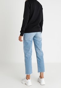 Svart sweatshirt, ljusblå raka jeans med fransig fåll, och vita sneakers. Tighta ärmar och avslappnad silhuett.