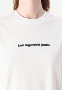 Balta medvilninė marškinėliai su juodu spausdintu logotipu "karl lagerfeld jeans" priekyje, apvaliu kaklu ir sklandžiu paviršiumi.