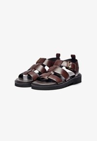 Brune lærsandaler med flere krydsremme, kraftig sort sål og en justerbar spænde detalje. Glat tekstur og åben design.