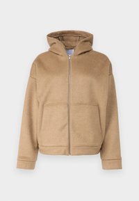 Beige zip-up hettegenser laget av myk stoff, med hette, frontlommer og brede mansjetter. Enkel design med en teksturert overflate.