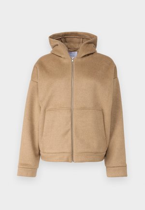 Kerged kapuutsiga pehme kangast beež vetthülgav tõmblukuga pusa, milles on ees taskud ja laiad varrukad. Lihtne disain tekstuurse viimistlusega.