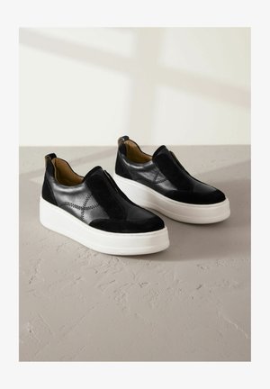 Fekete velúr és bőr slip-on cipők fehér platform talppal, dekoratív varrással és lekerekített orr kialakítással.