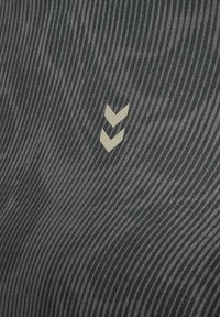 Zwei weiße nach unten zeigende Chevron-Symbole auf einem strukturierten dunkelgrauen Stoffhintergrund mit diagonalen Linien.