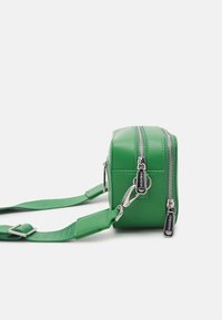 Zelená faux kůže crossbody taška s dvojitými stříbrnými zipy, nastavitelým popruhem, obdélníkovým tvarem a reliéfním logem na popruhu.