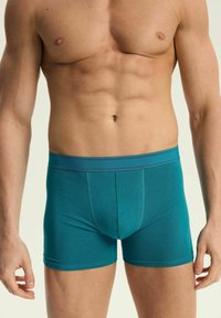 Turkusowe bokserki wykonane z gładkiego, elastycznego materiału, o dopasowanym kroju i kontrastowym pasie. Posiadają kieszeń do wsparcia.