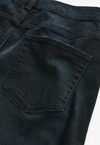 Donkerblauwe denim jeans met een achterzak met een gestikte rand en een gladde textuur. De stof heeft een lichte glans.