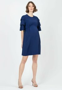 Tumm لباس بارداری رنگ نیوی آبی دارای آستینهای کوتاه با چینخوردگی ردیفی، یقه گرد و برش آزاد است که برای راحتی و آسایش طراحی شده است.