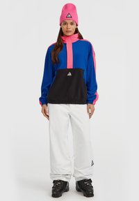 Blå og pink farvet blokeret pullover med høj krave, sort frontpanel, elastisk kant og et trekantet logo mærke. Sæt sammen med hvide snebukser.