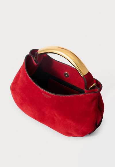 Crvena suede torba s zlatnim metalnim ručkama, strukturiranog oblika i crnim podstavom. Ima kopču na pritisak i utisnutu oznaku na vanjskoj strani.