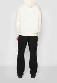 Bílá mikina s kapucí, s žebrovaným lemem. Ve spojení s černými cargo kalhotami s několika kapsami. Celý outfit doplňují tmavé boty.