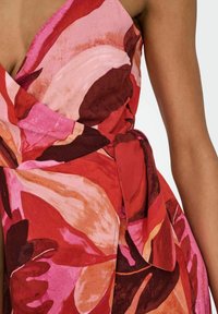 Abito avvolgente floreale rosso e rosa con scollatura a V profonda e dettaglio con fiocco laterale. Realizzato in tessuto morbido, presenta grandi motivi di foglie sovrapposte.