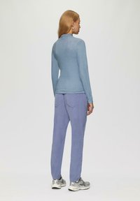 Helles blaues Langarmoberteil und helllila lässige Hose. Weiche Texturen mit glatter Oberfläche, ausgestattet mit Gesäßtaschen und silbernen Sneakers.
