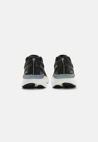Scarpe da ginnastica nere con una suola intermedia grigia e suola in gomma, caratterizzate da una tomaia in tessuto testurizzato e un branding minimale sul retro.
