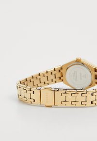 Gold metal watch with an octagonal face, link bracelet, and a clasp. Features a silver-toned back with brand logo, smooth finish.