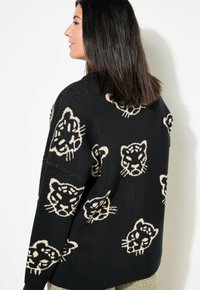 Mustapaita, jossa on beigellä neulottu leopardikuvio. Rentomallinen, löysä istuvuus, pitkät hihat ja pyöreä pääntie.