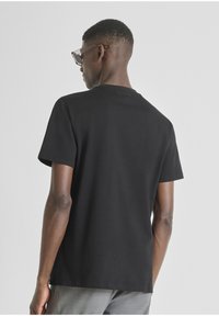 Crna majica kratkih rukava od pamuka, s okruglim izrezom i suptilnim logom na leđima. Glatka tekstura i klasičan kroj.