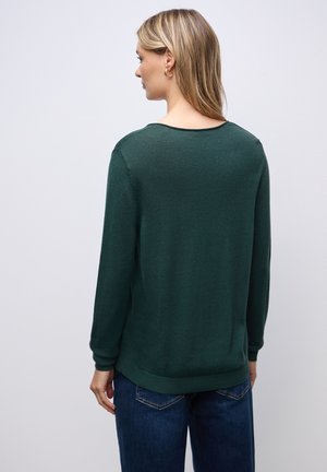 Grön tröja med långa ärmar, rundad halsringning, ribbade ärmslut och nederkant. Slät struktur med minimal detaljering, bärs med blå jeans.