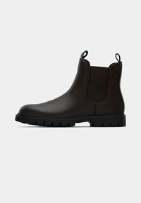 Bottine Chelsea en cuir marron foncé avec des panneaux élastiques noirs sur les côtés, des languettes de traction et une semelle épaisse en caoutchouc noir, présentée de profil sur fond blanc.