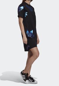 Svart oversized t-shirt klänning med reflekterande blå Adidas-logotryck. Matchas med svart och vita Adidas sneakers. Mjuk bomullskvalitet.