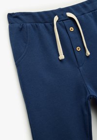 Pantalones de chándal azul marino con una tela texturizada, cintura con cordón, botones de madera y dos bolsillos laterales.