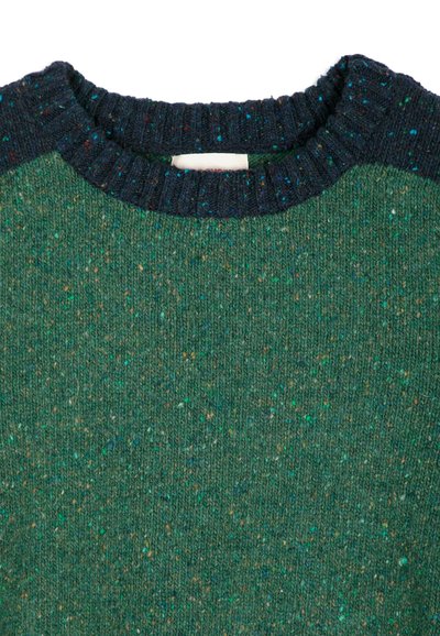 Gros plan d’un pull en maille vert avec un col côtelé bleu foncé et des taches multicolores sur tout le tissu.