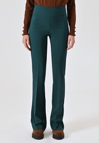 Pantaloni a vita alta color teal scuro, con una texture liscia, gambe diritte e dettagli minimi. Il modello indossa calzature marroni.