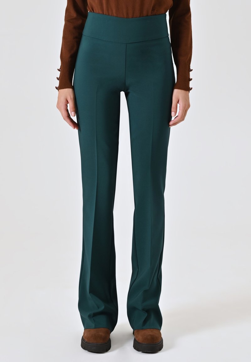 Pantaloni a vita alta color teal scuro, con una texture liscia, gambe diritte e dettagli minimi. Il modello indossa calzature marroni.