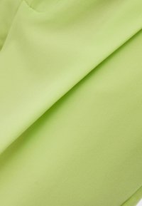 Tissu vert clair avec une texture lisse, présentant de subtilement plis et rides. Le matériau semble doux et légèrement extensible.