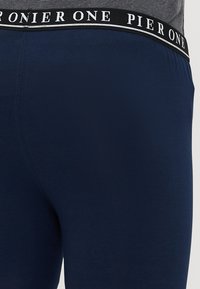 Ναυτικό μπλε κολάν με μαύρη μέση και λευκή επιγραφή "PIER ONE", κατασκευασμένα από λείο, απαλό ύφασμα με μέτρια εφαρμογή.