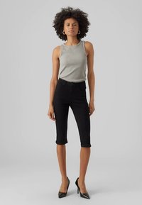 Gray sleeveless top paired with black knee-length jeans and black high heels. Smooth texture, fitted design, and minimal detailing.