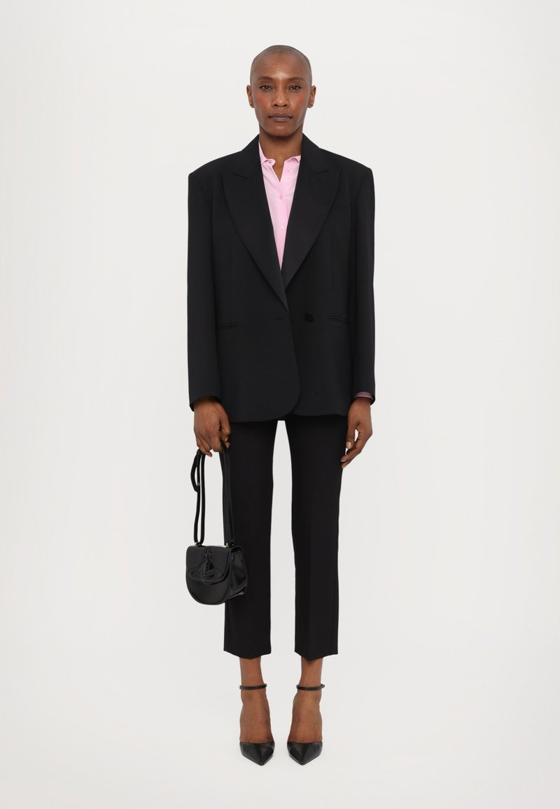 Czarny oversize blezer, różowa koszula, czarne dopasowane spodnie, czarne czółenka na szpilce i mała czarna torebka na pasek.