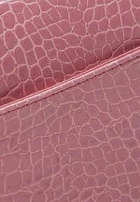 Pelle sintetica rosa con texture e motivo a pelle di rettile, caratterizzata da squame in rilievo e una cucitura lungo il bordo superiore.