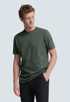 Donkergroene t-shirt met korte mouwen en een ronde halslijn, lichtgewicht textuur en subtiele logodetail op de borst, gecombineerd met zwarte broek.