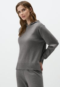 Grijze hoodie van zachte stof, heeft een ontspannen pasvorm, lange mouwen en een voorvak in kangoeroestijl. Zachte textuur met een geribde zoom.