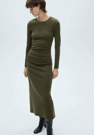 Long-sleeve green dress with a fitted silhouette, soft texture, crew neckline, and ruching detail at the waist, paired with knee-high black boots.